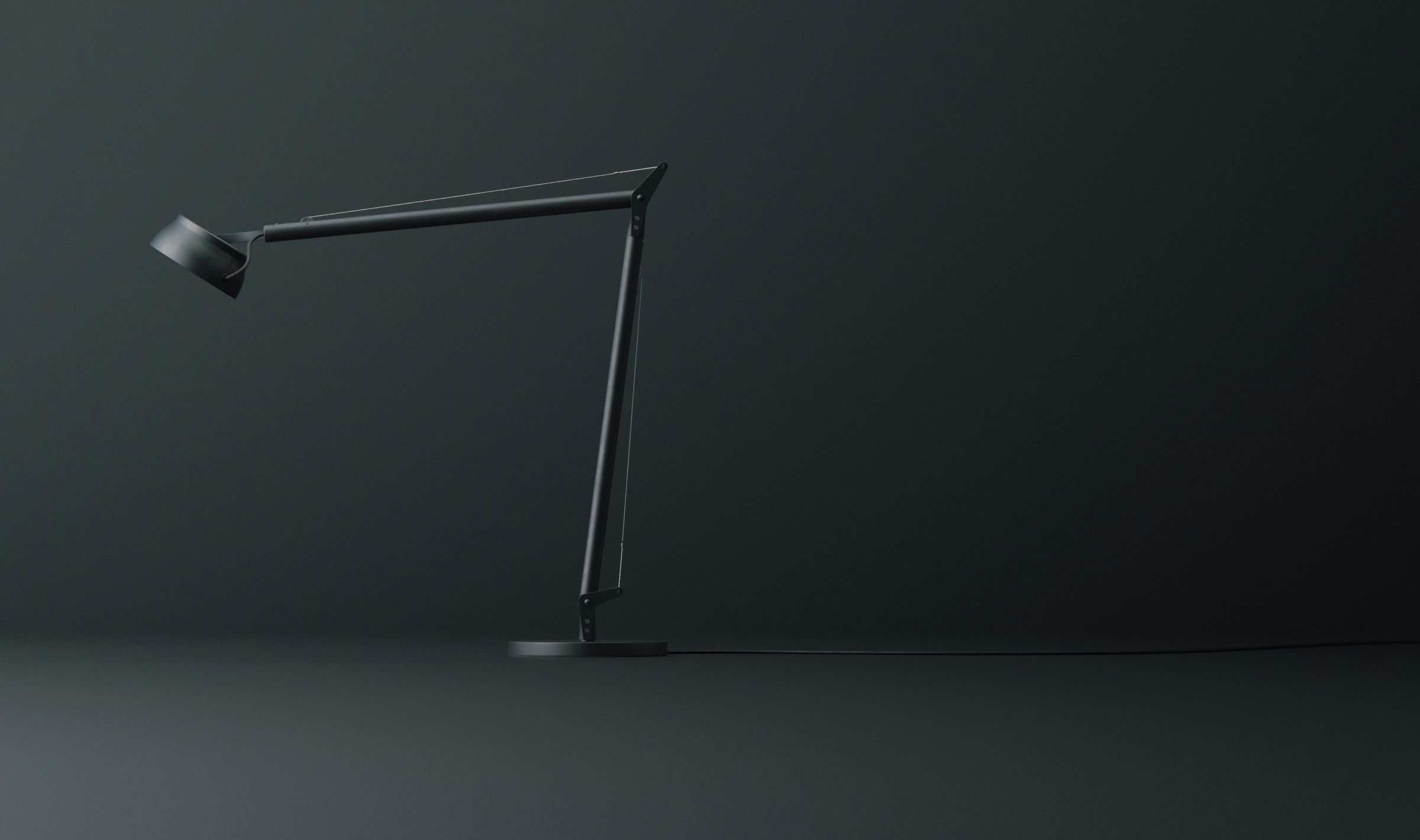 Side view of the finished matte black articulated task lamp, folded into a compact resting position against a dark studio background.
