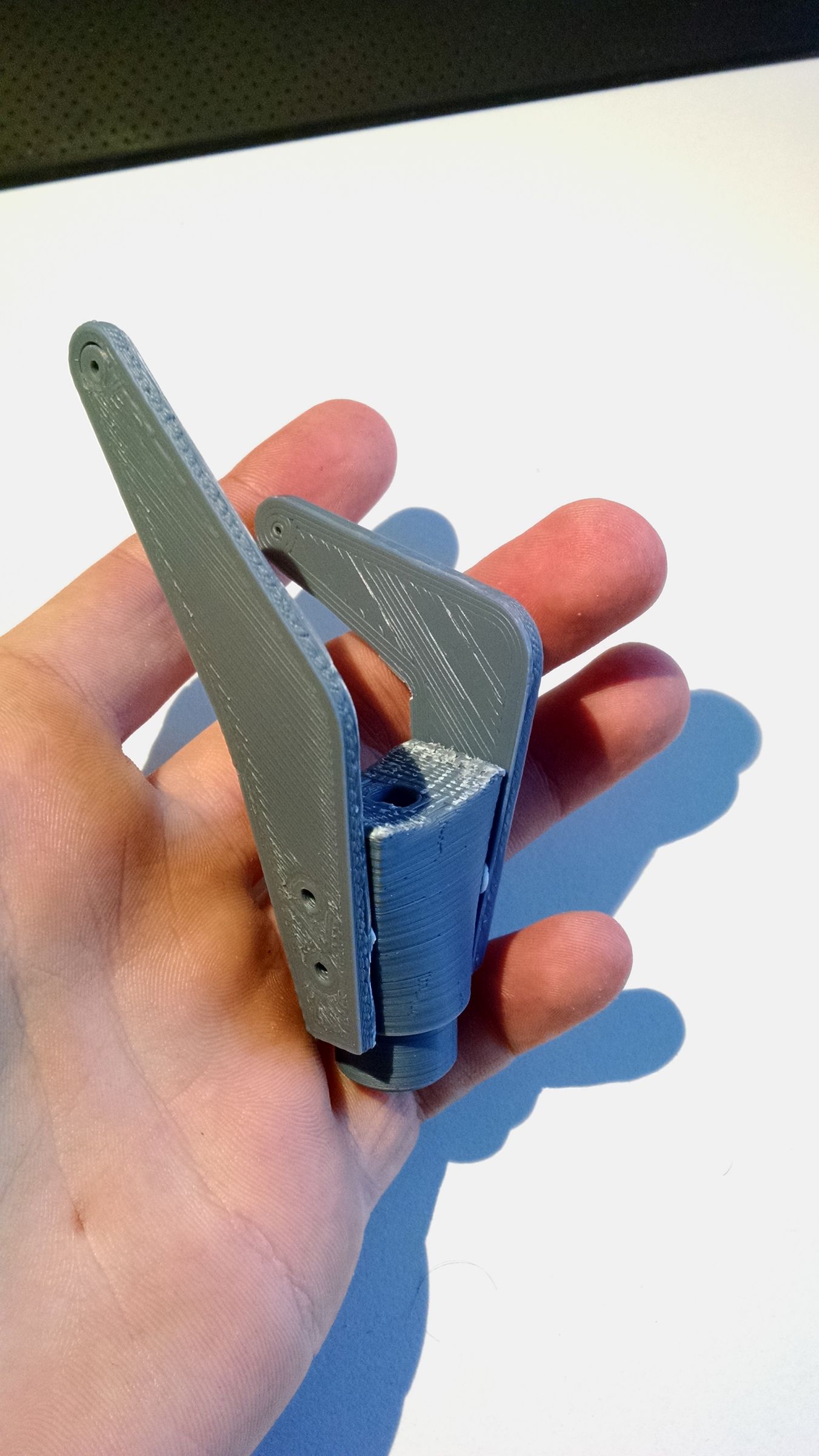 A hand holding a small grey 3D-printed hinge mechanism prototype against a white background.