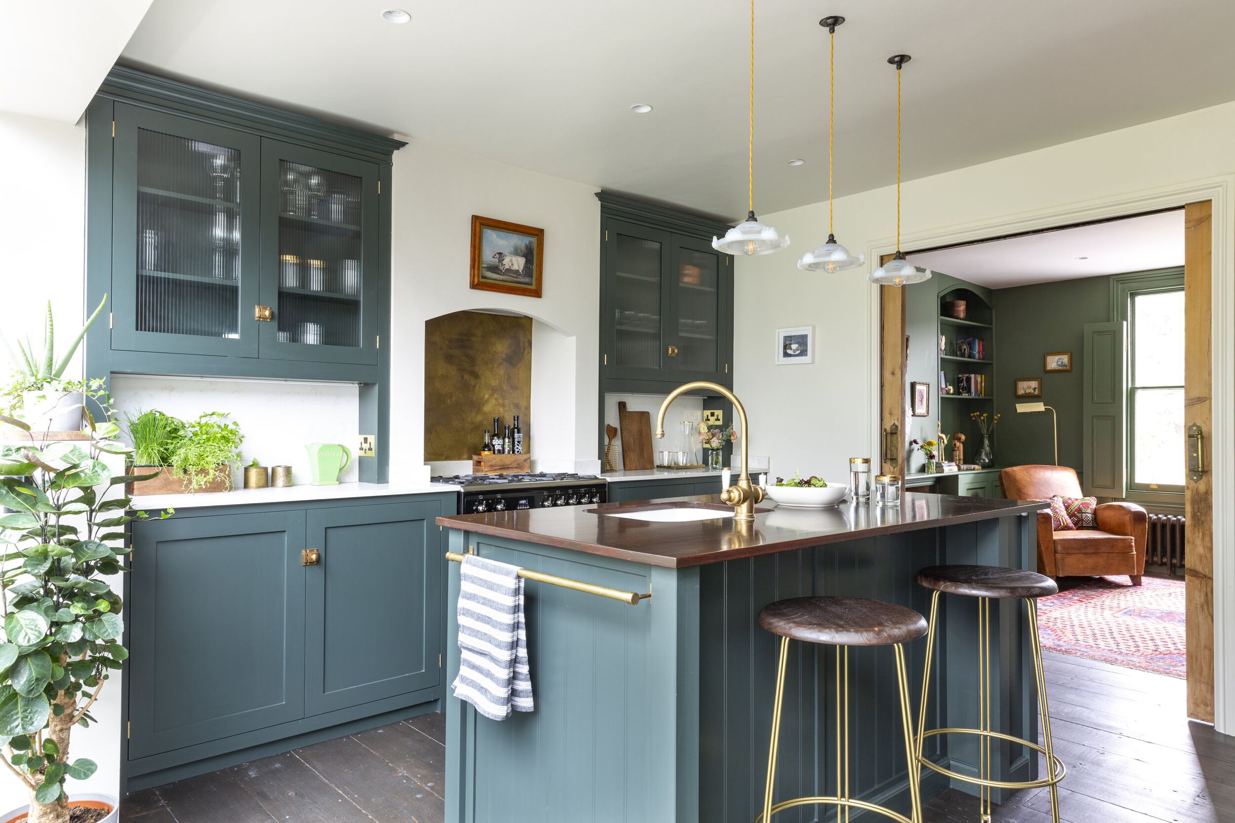 Photo of a green shaker style kitchen with a large island, brass accents, and a copper worktop.