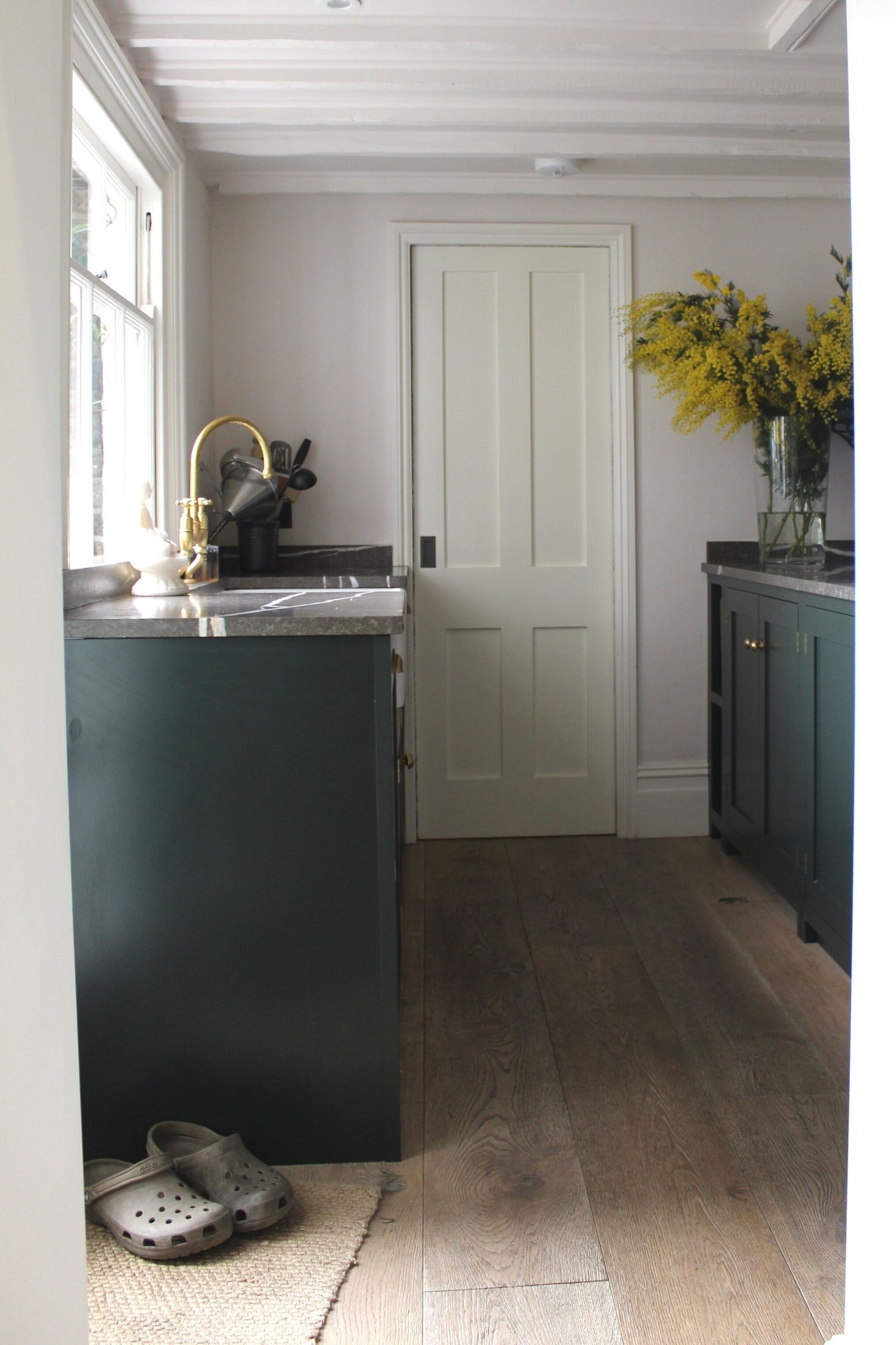 View of a dark green island unit with a corner sink, looking through to a white-panelled hallway beyond.